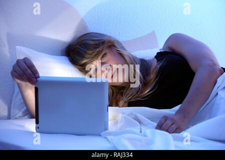 Giovane donna nel letto il surf con un iPad, tablet computer in internet tramite connessione wireless Foto Stock