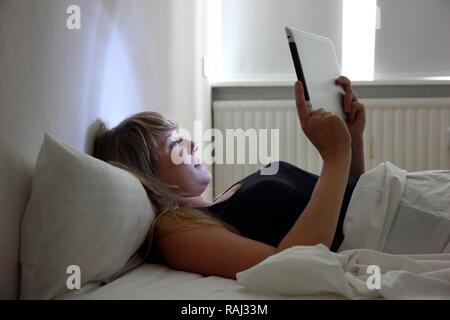 Giovane donna nel letto il surf con un iPad, tablet computer in internet tramite connessione wireless Foto Stock