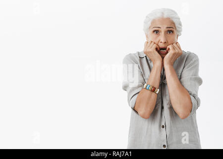 Vita-up shot di paura e in questione vecchia lonely lady sentirsi insicuro e tremante di paura holding palme vicino a bocca scendere in piedi preoccupati e spaventati contro uno sfondo grigio Foto Stock