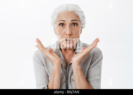 Vita-up shot di sollecite e sorpreso tipo nonna sensazione preoccupato e stupito holding palme vicino a volto alla ricerca in questione e interessa sapere cosa succede contro uno sfondo grigio Foto Stock