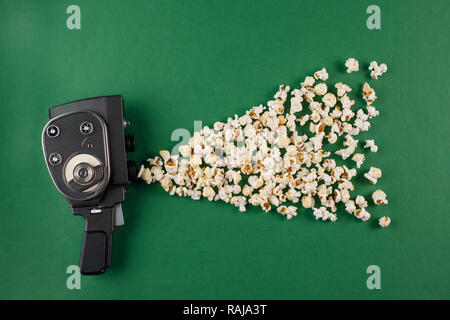 Retrò movie camera con pop-corn battenti fuori di esso su uno sfondo verde. Concetto di cinema. Foto Stock