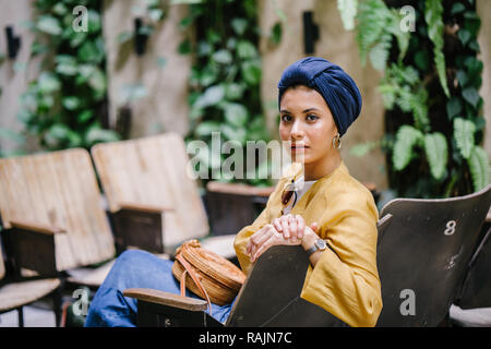 Un giovane medio donna orientale in un turban hijab è seduta e sorridente in un caffè di giorno in giorno. Lei è sorridente e felicemente è rilassato. Foto Stock