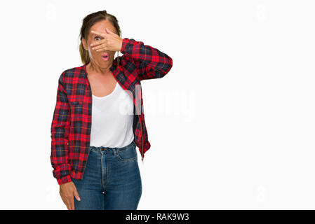 Medioevo donna adulta indossando giacca casual su sfondo isolato peeking in stato di shock che copre il viso e gli occhi con la mano, guardando attraverso le dita con Foto Stock
