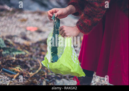 Una giovane donna è la pulizia di rifiuti di plastica sulla spiaggia Foto Stock