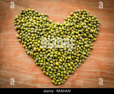 Fagioli di cuore / pila di fagioli di forma semi cuore verde su uno sfondo di legno nel fuoco selettivo Foto Stock