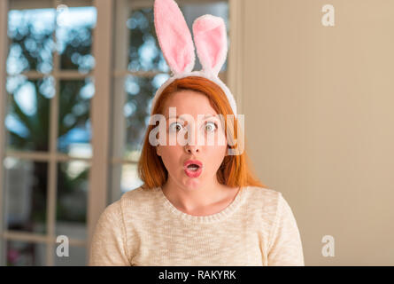 Redhead donna che indossa la pasqua orecchie di coniglio a casa spaventata in stato di shock con una faccia a sorpresa, paura e eccitati con espressione di paura Foto Stock