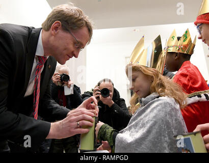 Kiel, Germania. 04 gen 2019. Daniel Günther (CDU), il primo ministro del Land Schleswig-Holstein, mette una banconota nella scatola di raccolta di un po' di star cantante. Circa 50 star cantanti da Schleswig-Holstein tradizionalmente benedisse la casa dello stato e la Cancelleria di Stato. Credito: Carsten Rehder/dpa/Alamy Live News Foto Stock