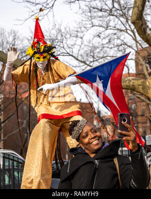 New York, Stati Uniti d'America. 4 gennaio 2019. Un esecutore su palafitte sventola una bandiera di Puerto Rico come una donna assume un selfie durante l'annuale quarantaduesima Tre Re parata del giorno El Barrio (East Harlem, New York City), organizzato da El Museo del Barrio, l'evento celebra la credenza popolare che tre uomini saggi visitato Gesù. Credito: Enrique Shore/Alamy Live News Foto Stock