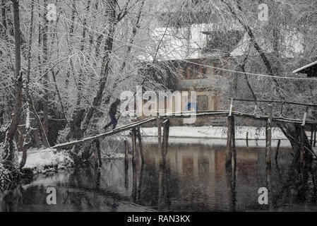 Uomo del Kashmir visto camminando su un ponte di legno coperto di neve durante la caduta di neve fresca a Srinagar. Nevicata nel lato indiano del Kashmir ha interrotto il traffico aereo e il traffico stradale tra Srinagar e Jammu, estate e inverno capitali dell India è stato Jammu-Kashmir, secondo le notizie. Foto Stock