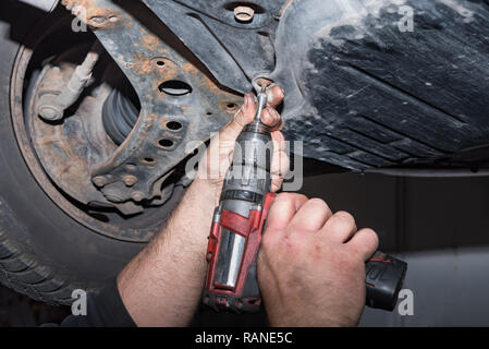 Meccanico al lavoro. Fissare la vite con il cacciavite a batteria. Lavorare nel negozio di riparazioni auto Foto Stock