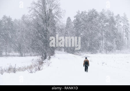 Ragazzo solitario strada a piedi al paesaggio invernale con la nevicata pesante in Finlandia Foto Stock