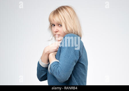 Una giovane donna europea nasconde qualcosa nelle sue mani e nel suo aspetto warily in avanti. Foto Stock