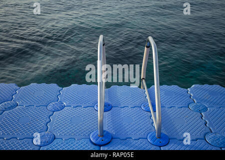 Bella la calma il mare blu di superficie di acqua in plastica e pontoon con scaletta che conduce in acqua. Orizzontale fotografia a colori. Foto Stock