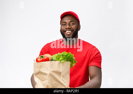 Concetto di consegna - Bello americano africano uomo consegna pacchetto portante negozio di generi alimentari il cibo e le bevande dal negozio. Isolato su grigio di sfondo per studio. Spazio di copia Foto Stock