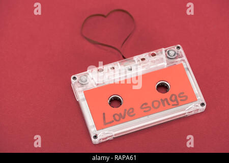 Vista ravvicinata della cassetta audio con scritte canzoni d'amore e il simbolo del cuore di fatto di nastro isolato sul rosso, san valentino concetto Foto Stock