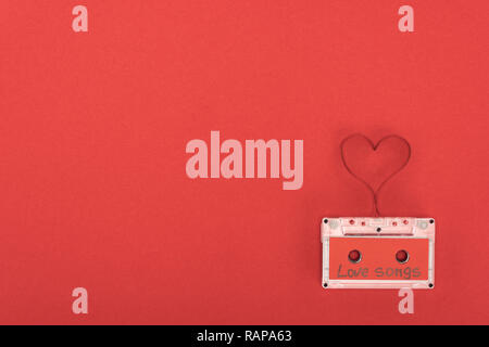 Vista in elevazione della cassetta audio con scritte canzoni d'amore e il simbolo del cuore di fatto di nastro isolato sul rosso, san valentino concetto Foto Stock