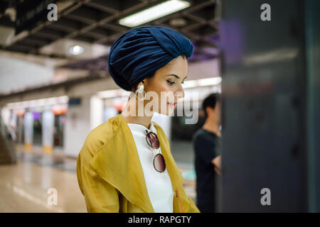 Una giovane e attraente donna musulmana in un velo e elegante color pastello vestiti è la consultazione di una mappa in una stazione ferroviaria per raggiungere la sua destinazione. Foto Stock