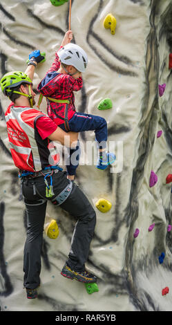 Istruttore maschio lavora con un giovane ragazzo sulla parete di arrampicata Foto Stock