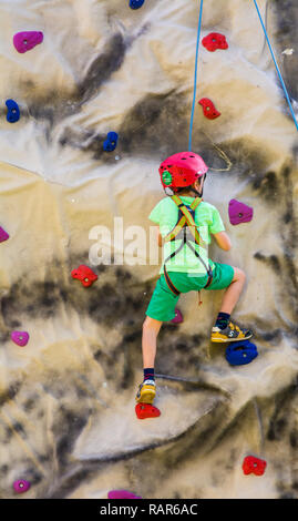 Colpo di Little Boy in un cablaggio salendo una parete con impugnature. Foto Stock