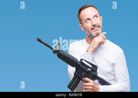 La mezza età senior annoso uomo delinquente tenendo la pistola arma isolato su sfondo faccia seriamente pensando di domanda, molto confusa idea Foto Stock