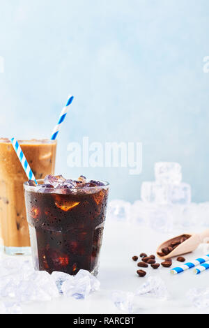 Estate bere caffè ghiacciato in un bicchiere di ghiaccio e caffè con la crema in un bicchiere alto, i chicchi di caffè e le cannucce circondato da ghiaccio su marmo bianco su tavola bl Foto Stock