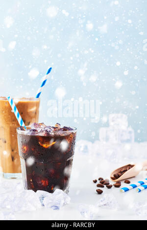 Inverno bere caffè ghiacciato in un bicchiere di ghiaccio e caffè con la crema in un bicchiere alto, i chicchi di caffè e le cannucce circondato da ghiaccio su marmo bianco su tavola bl Foto Stock