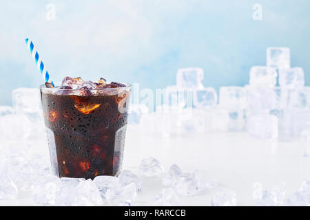 Estate bere caffè ghiacciato in un bicchiere con paglia circondati dal ghiaccio su marmo bianco tabella su sfondo blu. Messa a fuoco selettiva, copia spazio per il testo. Hor Foto Stock