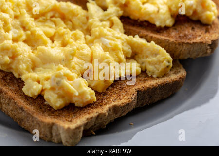 Close up di uova strapazzate su due pezzi di pane tostato su una lastra grigia su una semplice grigio e bianco sullo sfondo di marmo Foto Stock