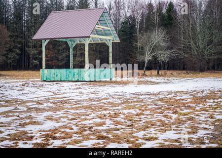 Il bisonte europeo e la foresta di vuoto gioco rack alimentazione con tetto metallico in Bialowieza, Polonia, parzialmente snow, verde hayrack, nuvoloso giorno di inverno Foto Stock