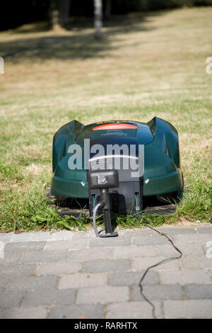 Verde robot automatico tosaerba inserito nella sua stazione di ricarica in prossimità di un patio, faccia a vista frontale Foto Stock