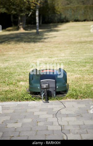 Verde robot automatico tosaerba inserito nella sua stazione di ricarica in prossimità di un patio, faccia a vista frontale Foto Stock