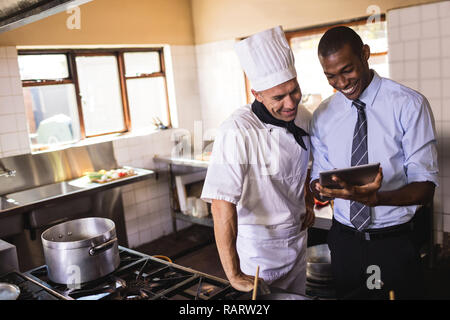 Maschio di manager e chef usando tavoletta digitale in cucina Foto Stock