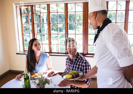 Lo chef serve cibo per coppia giovane seduto in un ristorante Foto Stock
