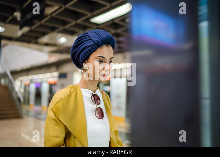 Una giovane e attraente donna musulmana in un velo e elegante color pastello vestiti è la consultazione di una mappa in una stazione ferroviaria per raggiungere la sua destinazione. Foto Stock