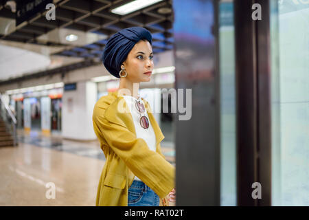 Una giovane e attraente donna musulmana in un velo e elegante color pastello vestiti è la consultazione di una mappa in una stazione ferroviaria per raggiungere la sua destinazione. Foto Stock