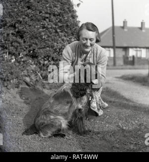 Degli anni Cinquanta, storico su un orlo erbosa, una matura signora inglese inginocchiato accanto al suo cane, un Cocker Spaniel. Foto Stock