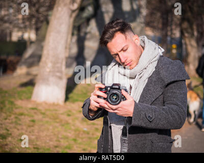 Bel giovane maschio fotografo o videomaker riprese video riprese con videocamera professionale, all' aperto nel parco della città Foto Stock