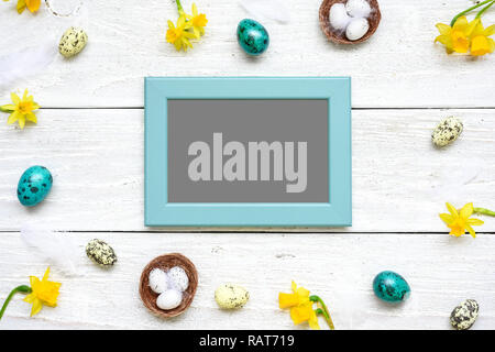 Blank Foto scheda nella cornice fatta di uova di quaglia, fiori di primavera e piume bianche su sfondo di legno. Composizione di pasqua. vista superiore con spazio di copia Foto Stock