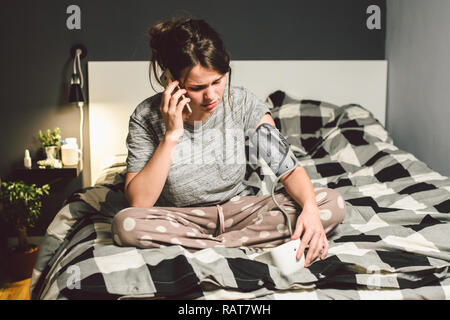 L'argomento di alta pressione sanguigna di ipertensione malattia. Bella giovane donna utilizza il tonometro automatico per controllare la pressione a casa in camera da letto sul letto Foto Stock