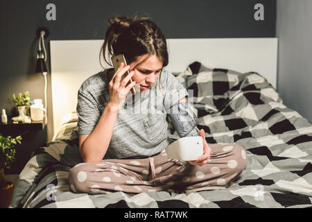 L'argomento di alta pressione sanguigna di ipertensione malattia. Bella giovane donna utilizza il tonometro automatico per controllare la pressione a casa in camera da letto sul letto Foto Stock