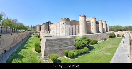 La facciata con torri e mura di islamica del Castillo de la Aljafería fortezza, con prato e piante nel fossato giardino, in una soleggiata estate, in Zaragoza, Spagna Foto Stock