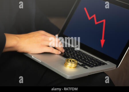 Imprenditore lavorando sul computer portatile con un golden bitcoin monete pila su di esso. Il grafico rosso, il crollo dei prezzi del concetto. Foto Stock