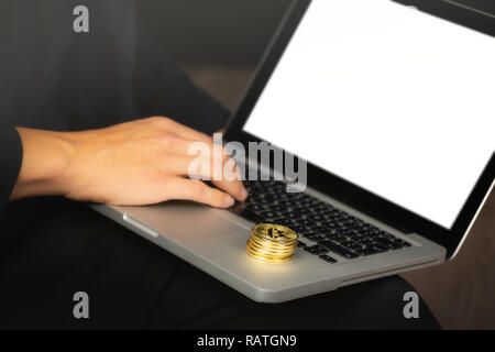 Imprenditore lavorando sul computer portatile con un golden bitcoin monete pila su di esso. Bianco schermo vuoto. Foto Stock