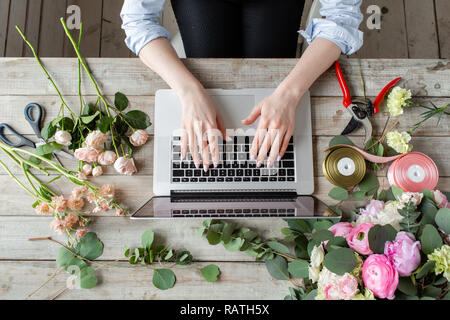Close-up di mani, tastiera portatile e tavola floreale. La donna blogger e creatori di contenuti di social network e blog negozio di fiori. Il concetto di negozio online e di consegna floreale. SMM promozione Foto Stock