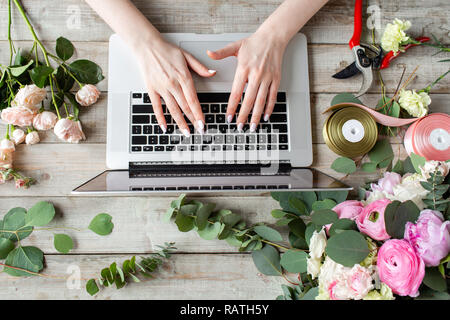 Close-up di mani, tastiera portatile e tavola floreale. La donna blogger e creatori di contenuti di social network e blog negozio di fiori. Il concetto di negozio online e di consegna floreale. SMM promozione Foto Stock