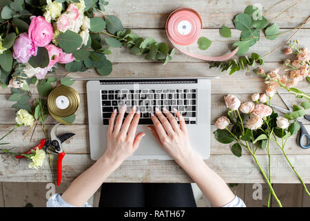 Close-up di mani, tastiera portatile e tavola floreale. La donna blogger e creatori di contenuti di social network e blog negozio di fiori. Il concetto di negozio online e di consegna floreale. SMM promozione Foto Stock