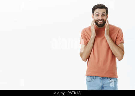 L'uomo sensazione di sorpresa e felice cercando in mirror godendo nuovo look. Bel lieto europeo maschio barbuto toccando il viso e sorridendo con gioia e soddisfazione che pongono contro uno sfondo bianco Foto Stock