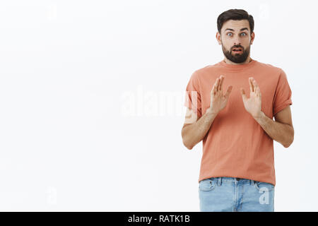 Wow rallentare. Preoccupato e nervoso fidanzato ha paura delle responsabilità che vogliono prendere un passo indietro con la relazione solleva le palme in stop e gesto di rifiuto alla ricerca solleciti a fotocamera sulla parete grigia Foto Stock