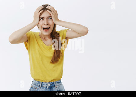 Donna sensazione di panico preoccupati e turbati tenendo le mani sulla testa dal panico urla turbato e interessati, accigliata e guardando con terrore espressione nervoso in posa sulla parete grigia Foto Stock