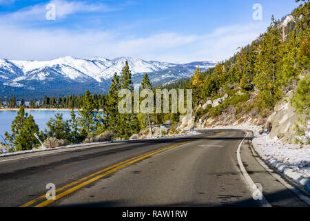 Viaggiando sulla riva del lago di Tahoe su una giornata invernale; Sierra montagne coperte di neve visibile in background Foto Stock